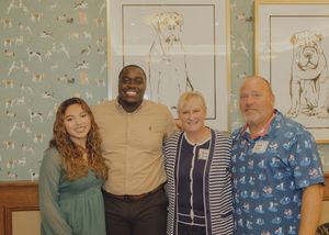 Four people smiling together posed in front of dog-themed wallpaper and framed dog portraits.