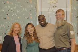 Four adults posing together smiling in front of decorative dog-themed wallpaper at an event.