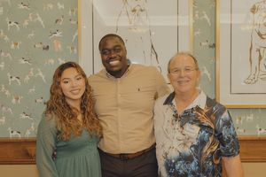 Three smiling friends posing together indoors, with decorative wall art featuring animals in the background.