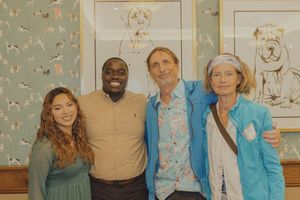 Four people pose together smiling in a room featuring teal dog-themed wallpaper and framed dog art.