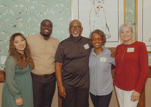 Five people smiling and posing together at an indoor event, standing in front of a decorative wall mural.