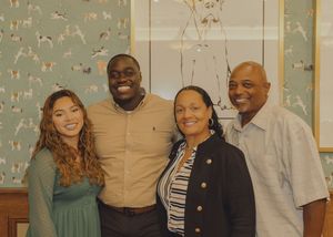 Four people smiling together for a group photo in front of dog-themed wallpaper and artwork.