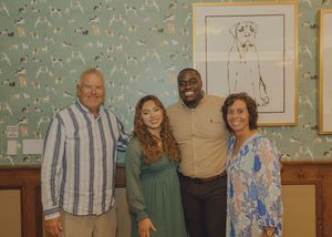 Four people pose together smiling in front of framed dog wall art.
