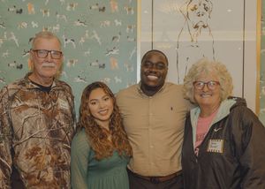 Four people smiling together indoors in front of a decorative wall mural, posing for a group photo.