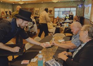 A magician in a top hat performs a card trick for seated guests at an event.