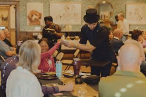 A magician in a top hat performs a trick for seated guests at an elegant indoor dining event.