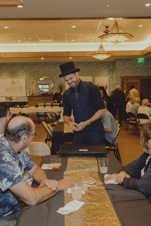 A magician in a top hat entertains seated guests at a banquet hall event.