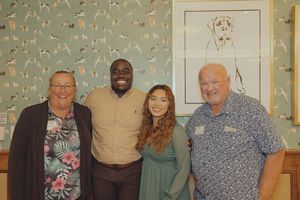 Four people smiling together in a room with dog-themed wallpaper and framed dog artwork.