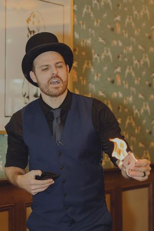 A magician in a top hat performs a fire trick at an indoor social event.