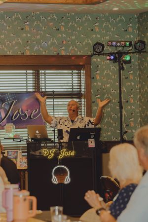 DJ Jose energetically performs at a party setup with DJ equipment, lights, and dog-themed wallpaper.