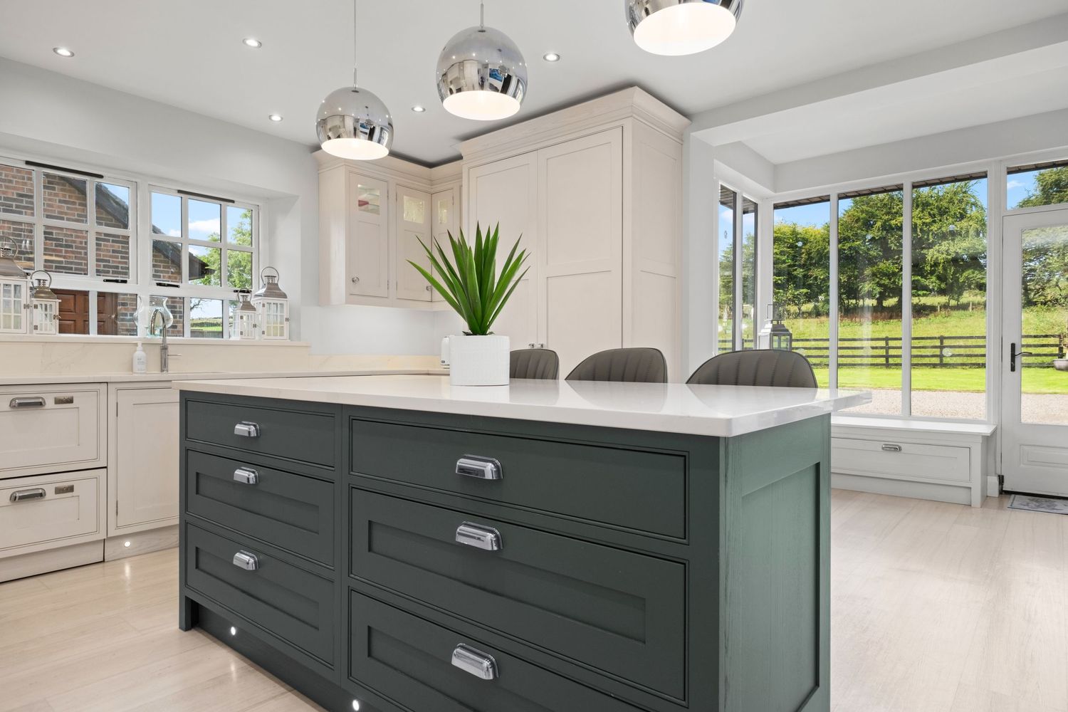 Stylish kitchen with dark green island, white cabinetry, marble countertops, and bifold doors opening to garden views.