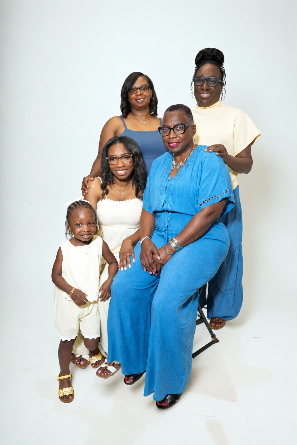 Four generations of women and a young girl pose together in a studio family portrait, wearing coordinated blue and cream outfits.