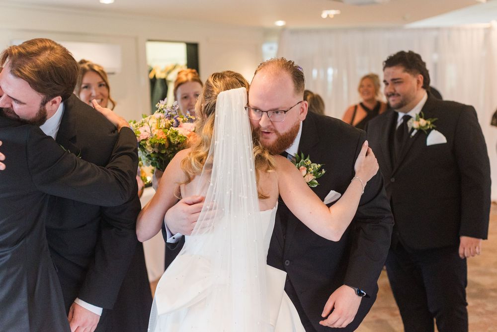 Bride and groom sharing an emotional hug with wedding guests during indoor wedding reception ceremony.