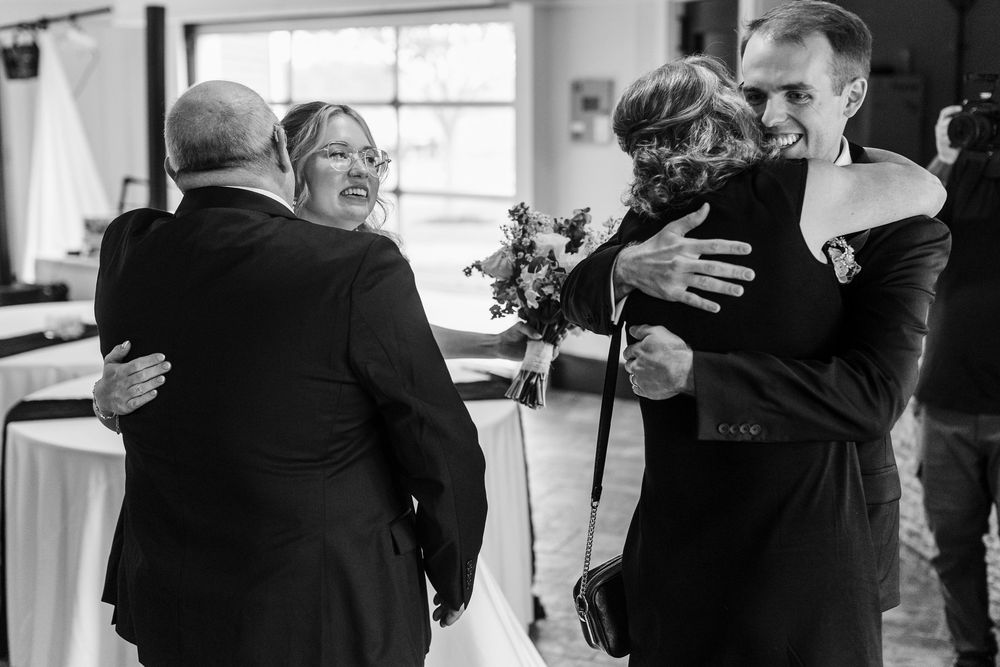 Black and white wedding photo of guests exchanging warm hugs and embraces during a reception celebration.