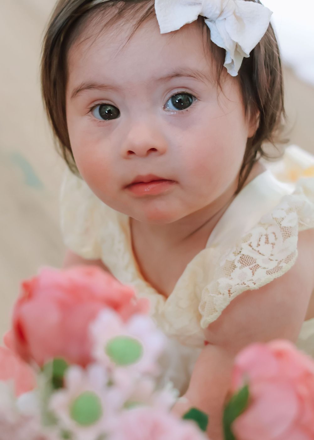 Close-up of a baby girl with a white bow surrounded by pink flowers, NJ first birthday photographer