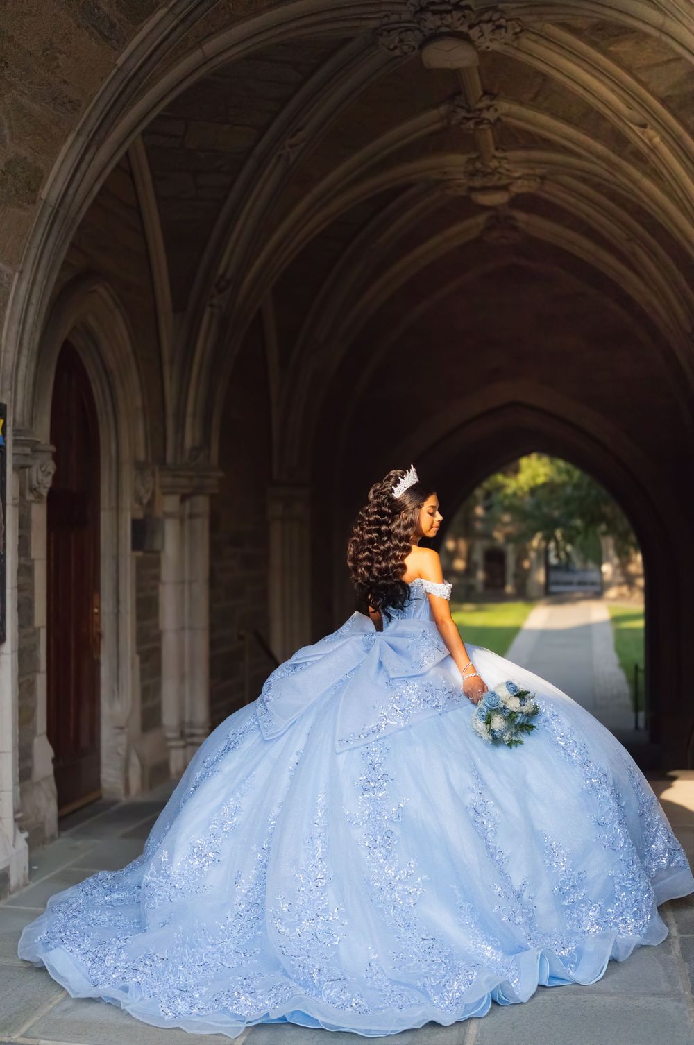 Teen in a light blue ball gown under a gothic stone archway, quinceañera photos in Princeton, NJ
