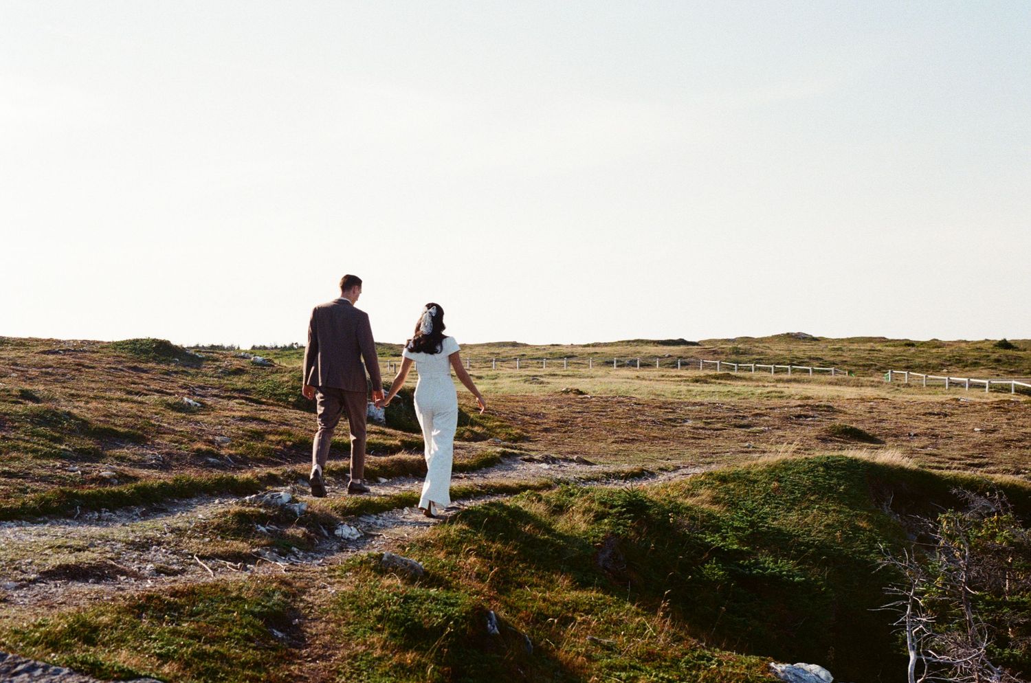 bride and groom walk along a trail in a grassy meadow