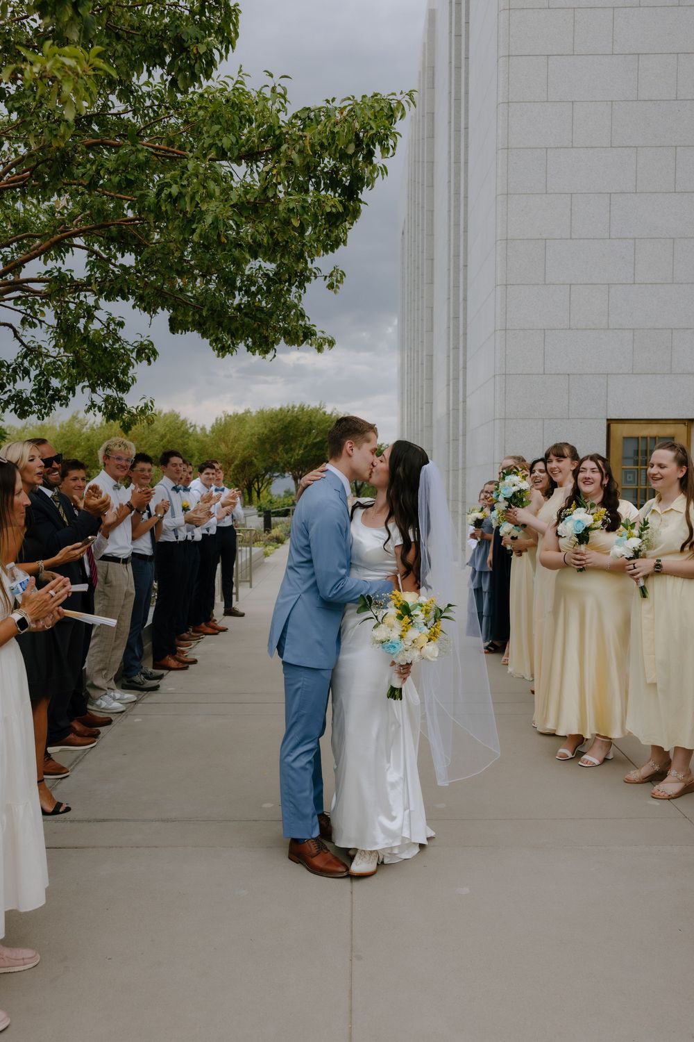 Bride and groom share a first kiss as wedding guests applaud outside a stone temple.