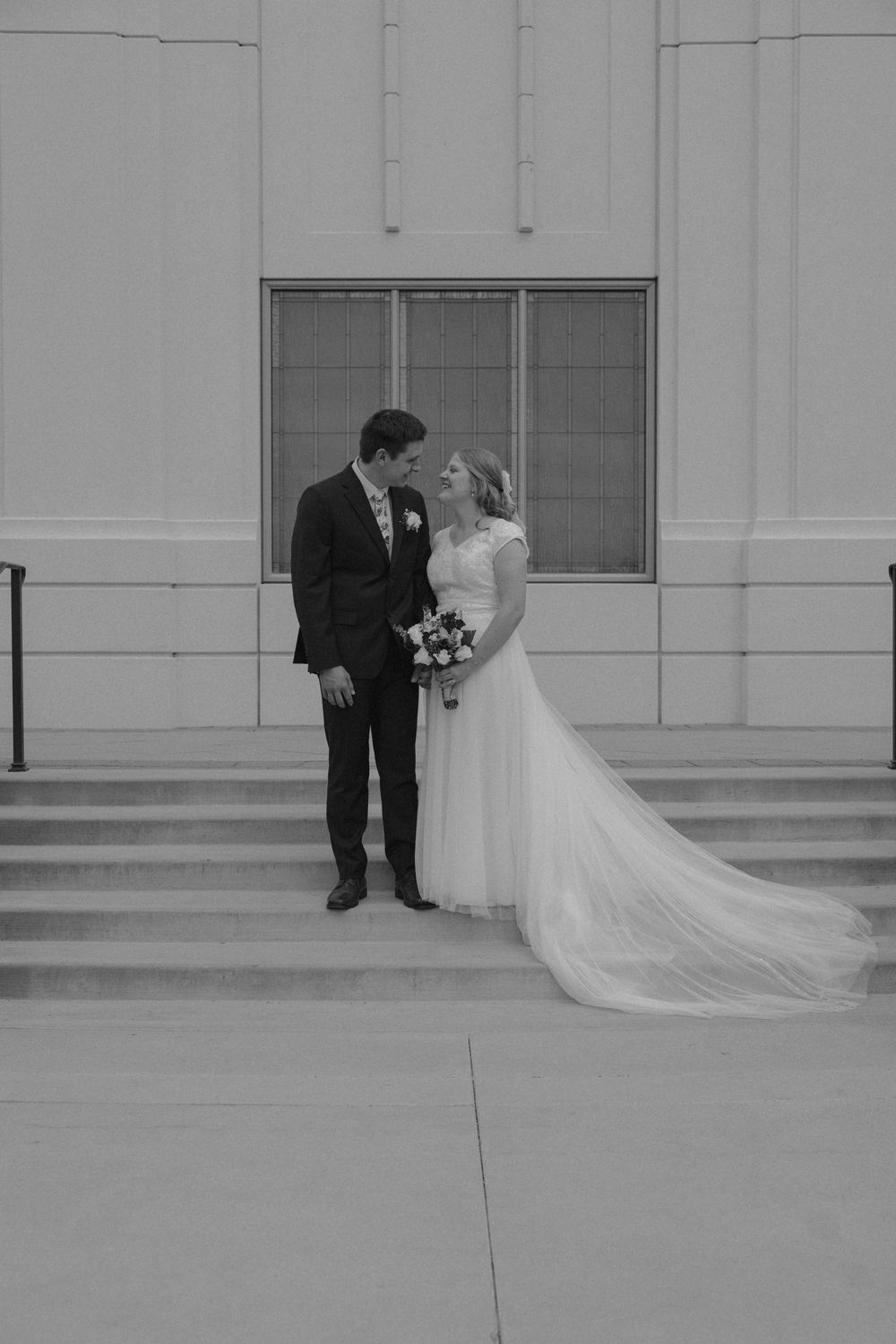 Black and white photo of bride and groom sharing romantic moment on steps outside wedding venue.
