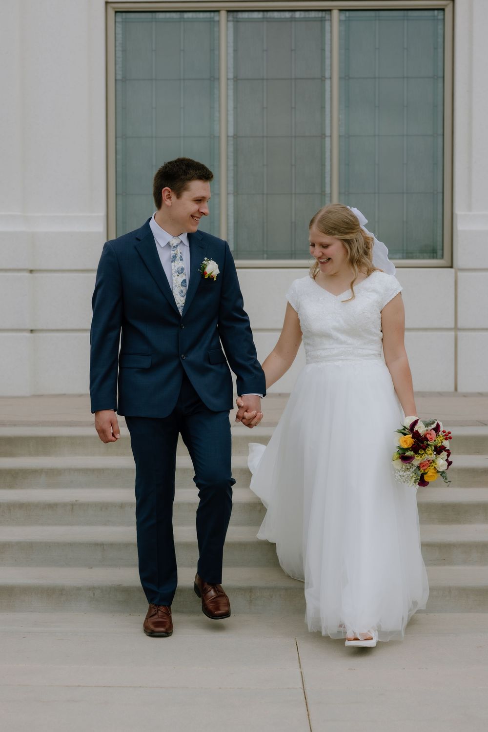 Bride and groom holding hands walking down temple steps on their wedding day.