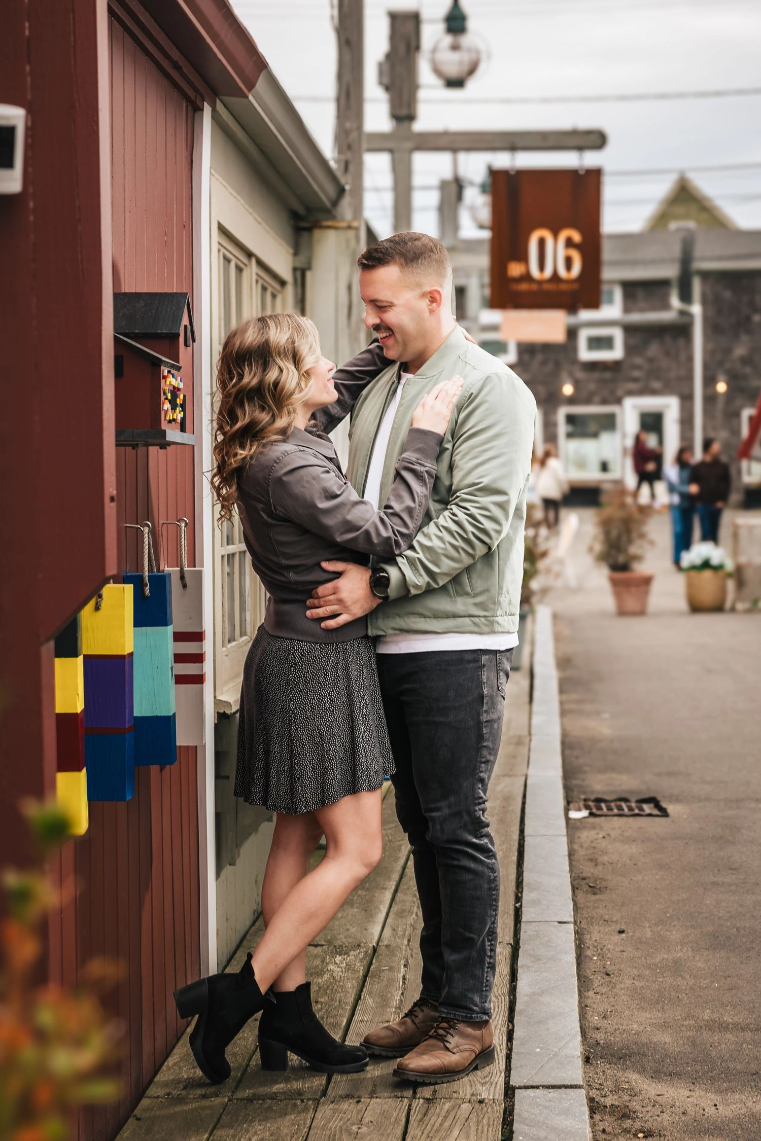 Couple embracing and gazing at each other against a brick building wall in a town street. Engagement at Rockport Harbor, Rockport, MA
