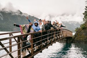 Group of travelers posing on a wooden bridge over a river with misty mountains in the background. Captured by Savvy Photography
