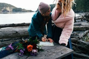 A couple signing documents on a driftwood table by the water, at Deception Pass, WA during an elopement Captured by Savvy Photography