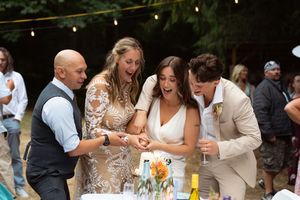 Two bride and to grooms cut the cake together at a backyard wedding reception Captured by Savvy Photography