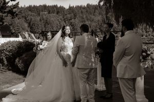 Black and white outdoor wedding ceremony with bride in ball gown and veil exchanging vows with groom. Captured by Savvy Photography