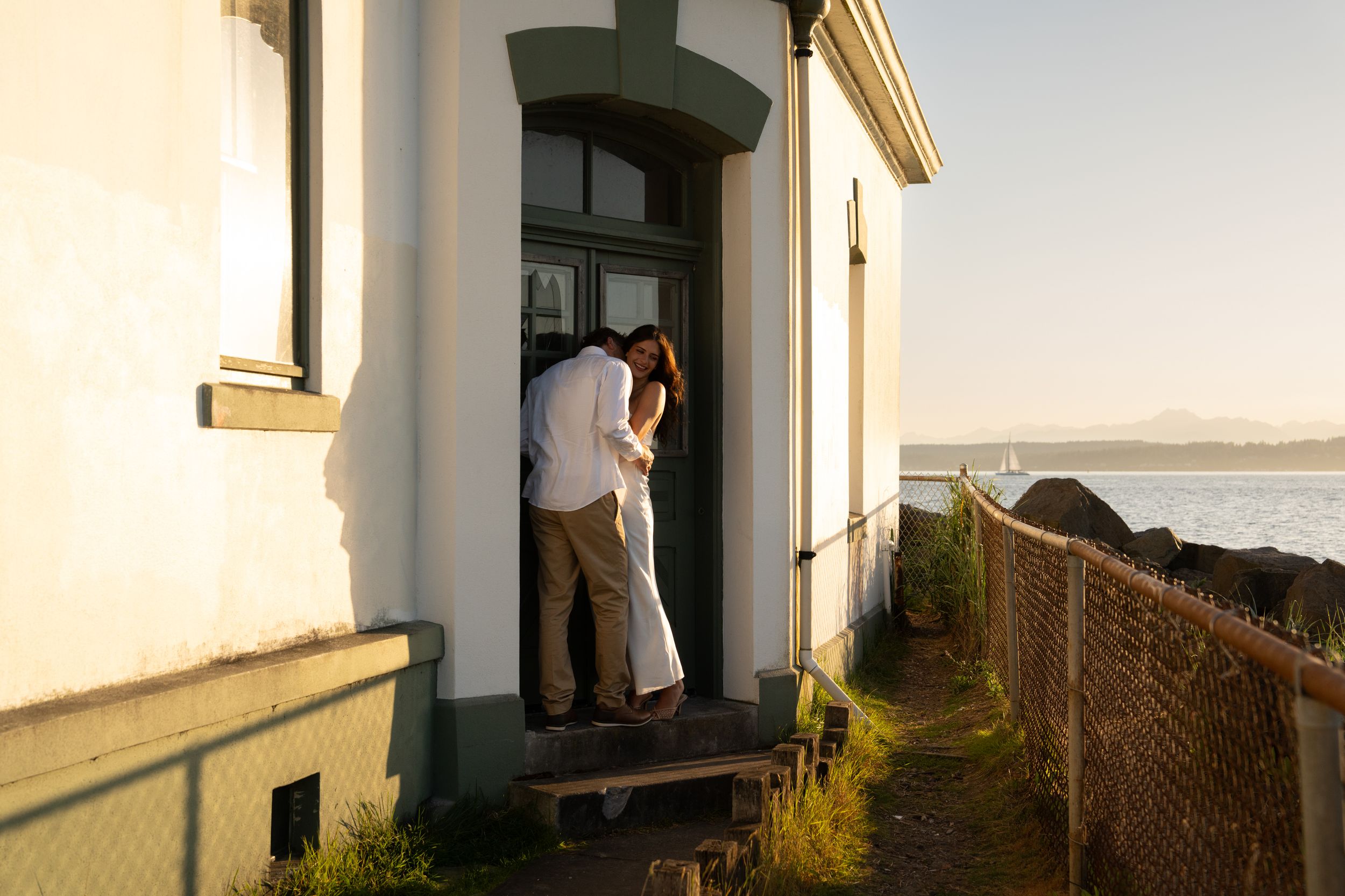 Couple embracing in a doorway of a coastal building at golden hour with ocean views in the background.