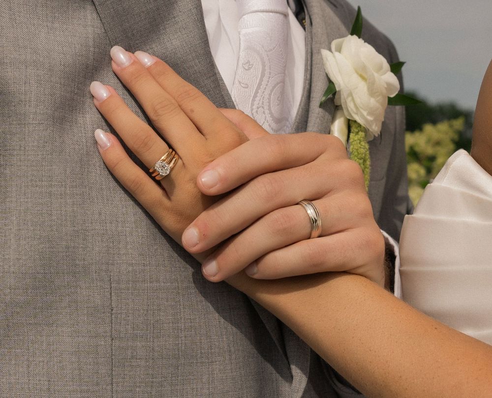 Newlywed couple displaying wedding rings, bride wearing diamond engagement ring and groom with silver band on their hands.