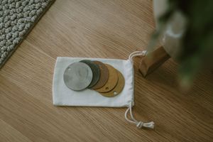 Circular leather and concrete coasters in a white drawstring pouch on a wooden floor.