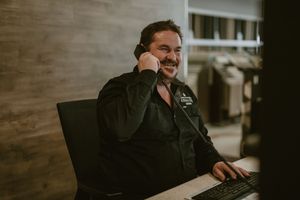 Smiling man talking on phone while working at a computer desk in a modern office setting.