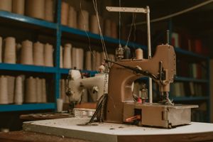 Vintage brown sewing machine on a workbench in a textile workshop with spools of thread on shelves.