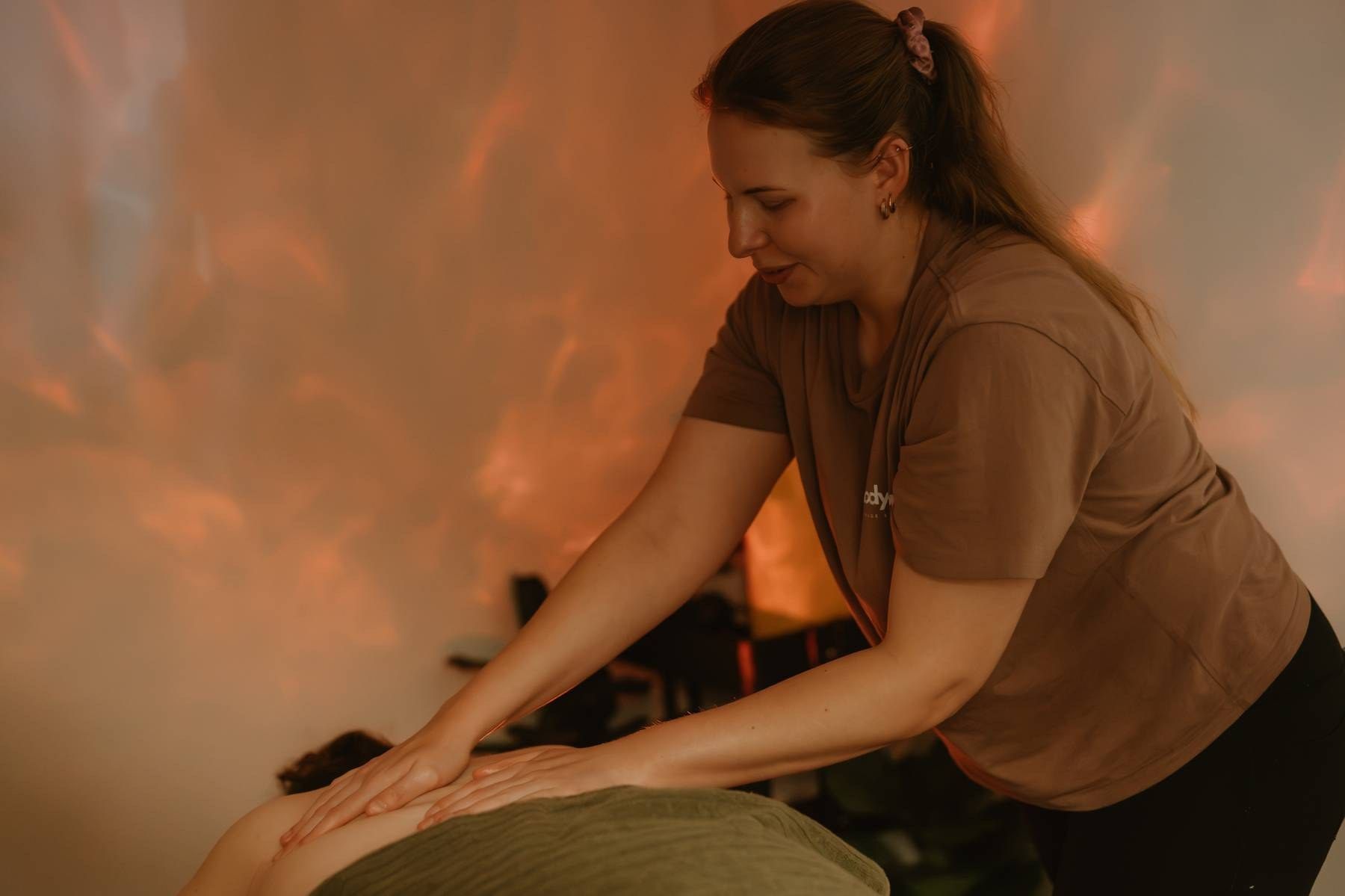 A massage therapist performs a relaxing back massage in a warmly lit spa room with glowing amber walls.