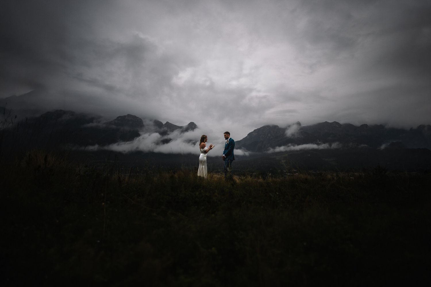 Couple stands on misty mountain meadow under dramatic stormy clouds during their outdoor wedding elopement.