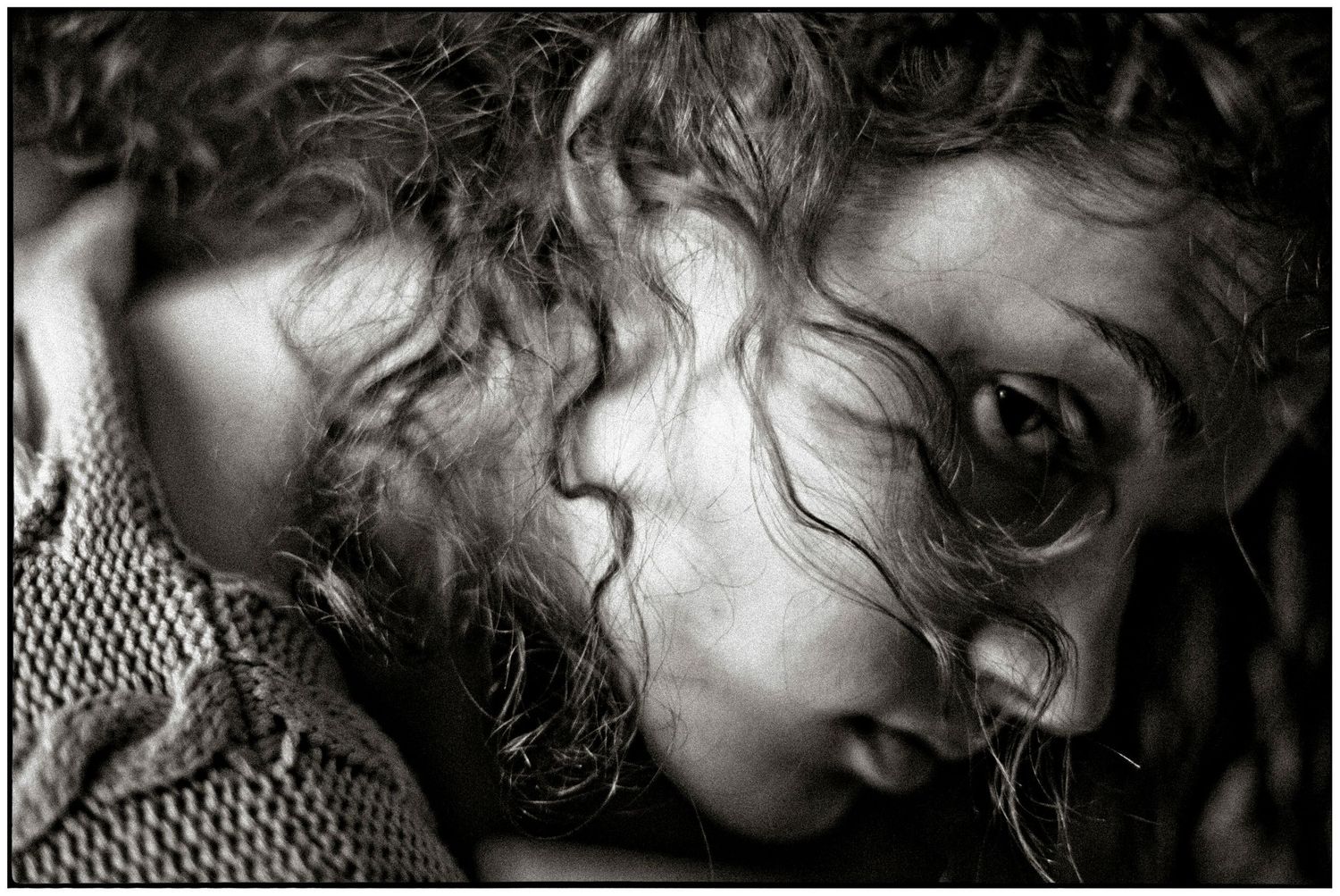 Black and white portrait of a young woman with curly hair, gazing pensively with a dramatic, artistic composition.