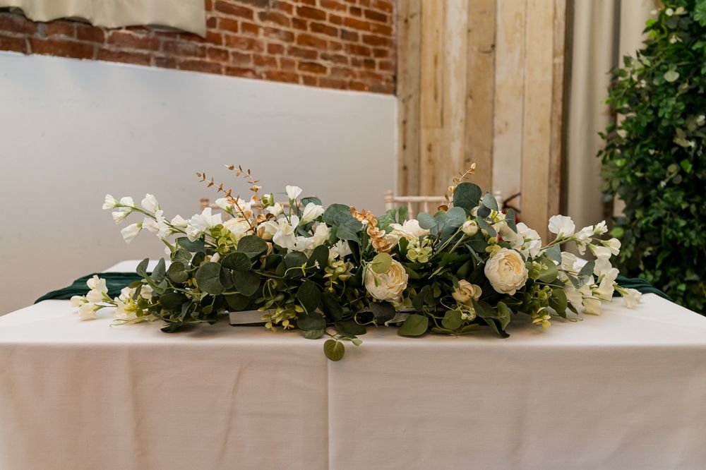 Elegant wedding table centerpiece with white roses, greenery, and eucalyptus on a white linen tablecloth.