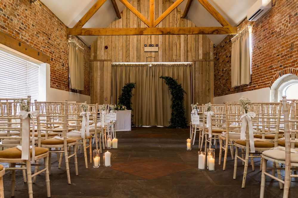 Elegant barn wedding venue with chiavari chairs, candlelit aisle, exposed brick walls, and floral arch backdrop.