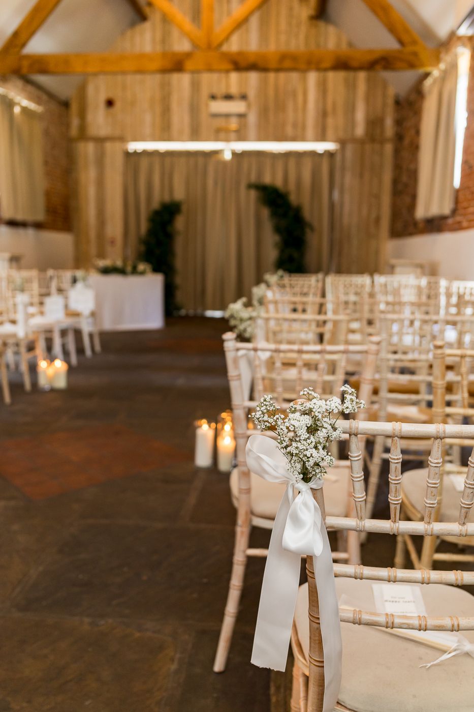 Elegant barn wedding ceremony with chiavari chairs, baby's breath bouquets, white ribbon, and candles lining the aisle.