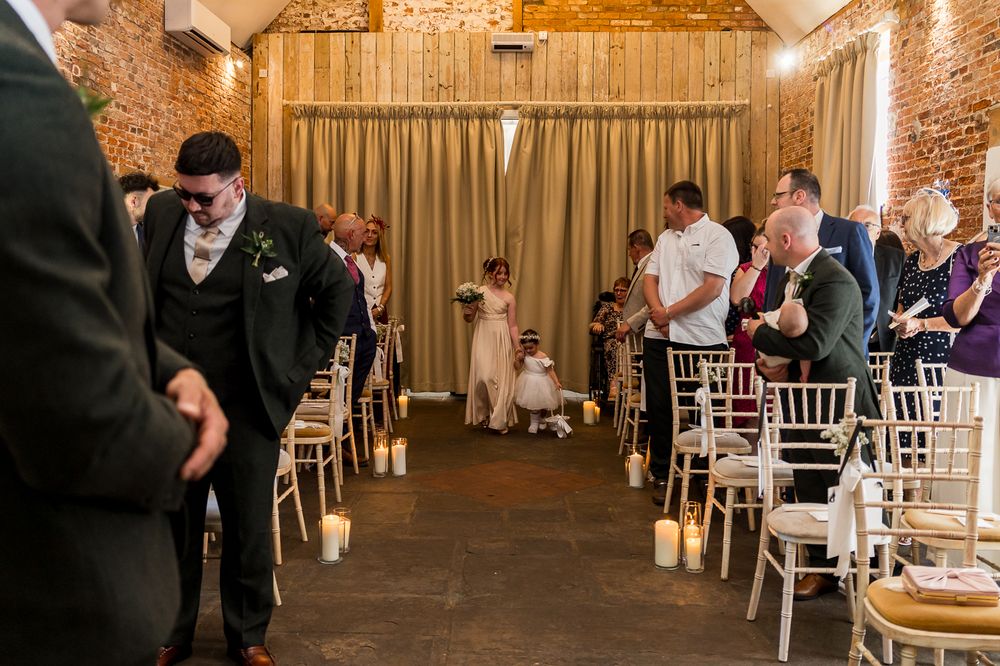 Elegant wedding ceremony in a rustic brick venue with guests seated on white chairs lining the aisle.