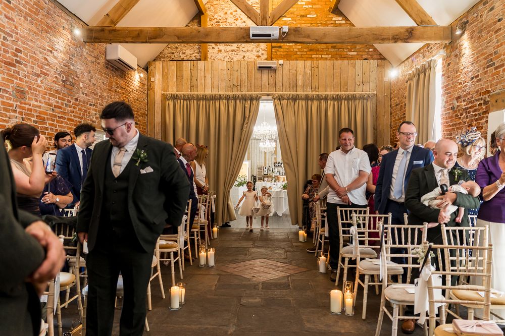 Groom stands at the altar awaiting his bride in a candlelit rustic brick wedding ceremony venue.