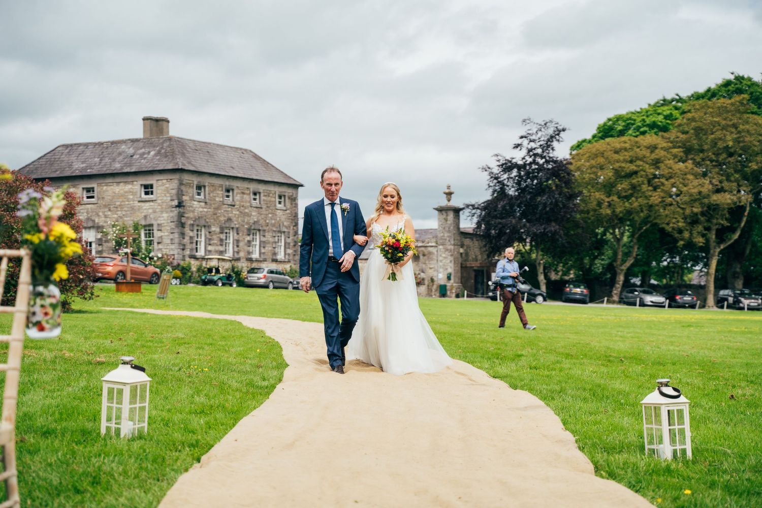 Bride and groom walking down outdoor aisle at Irish country house wedding venue on a cloudy day at Bellinter house