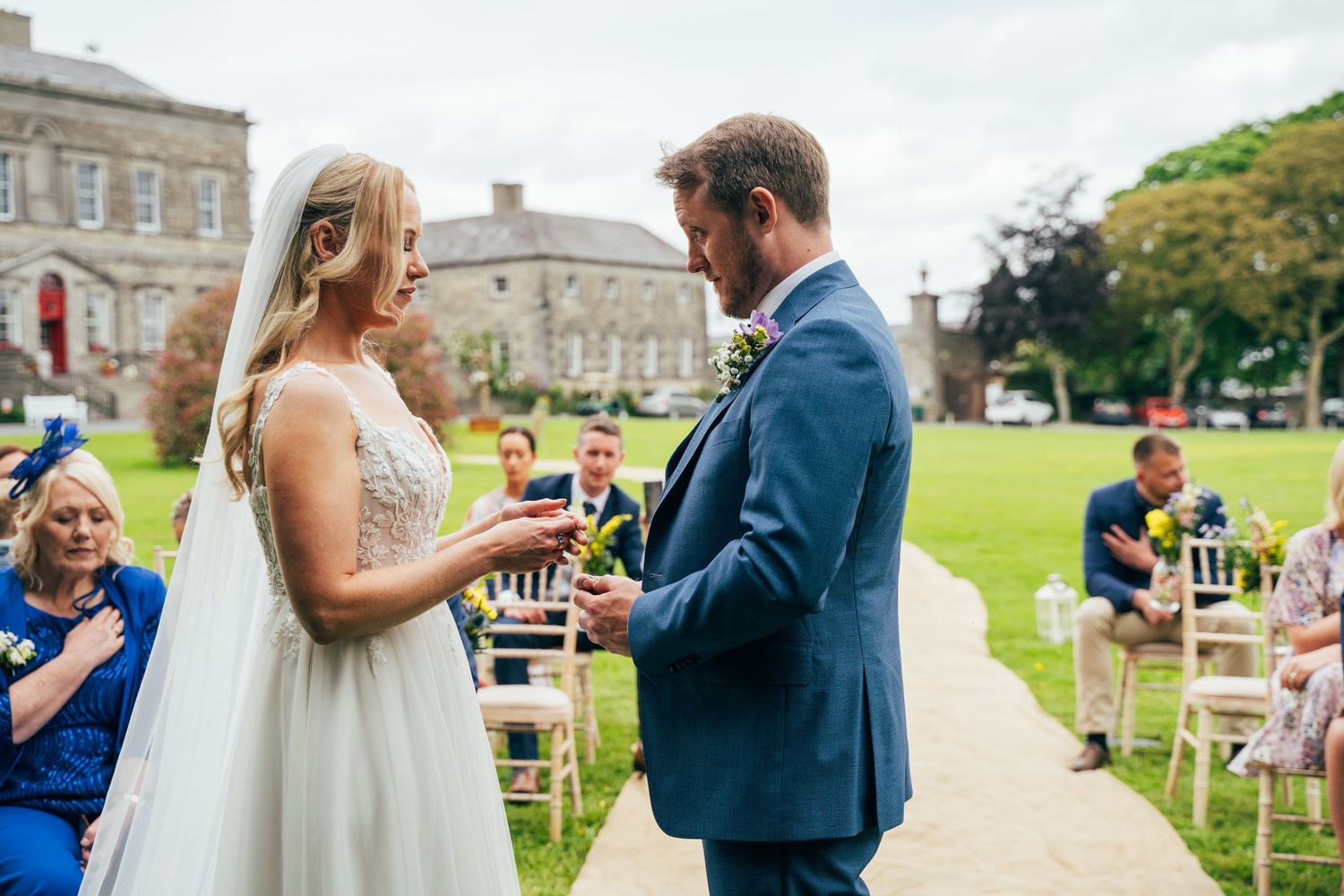 Bride and groom exchange rings during outdoor wedding ceremony on green lawn with historic  Bellinter house