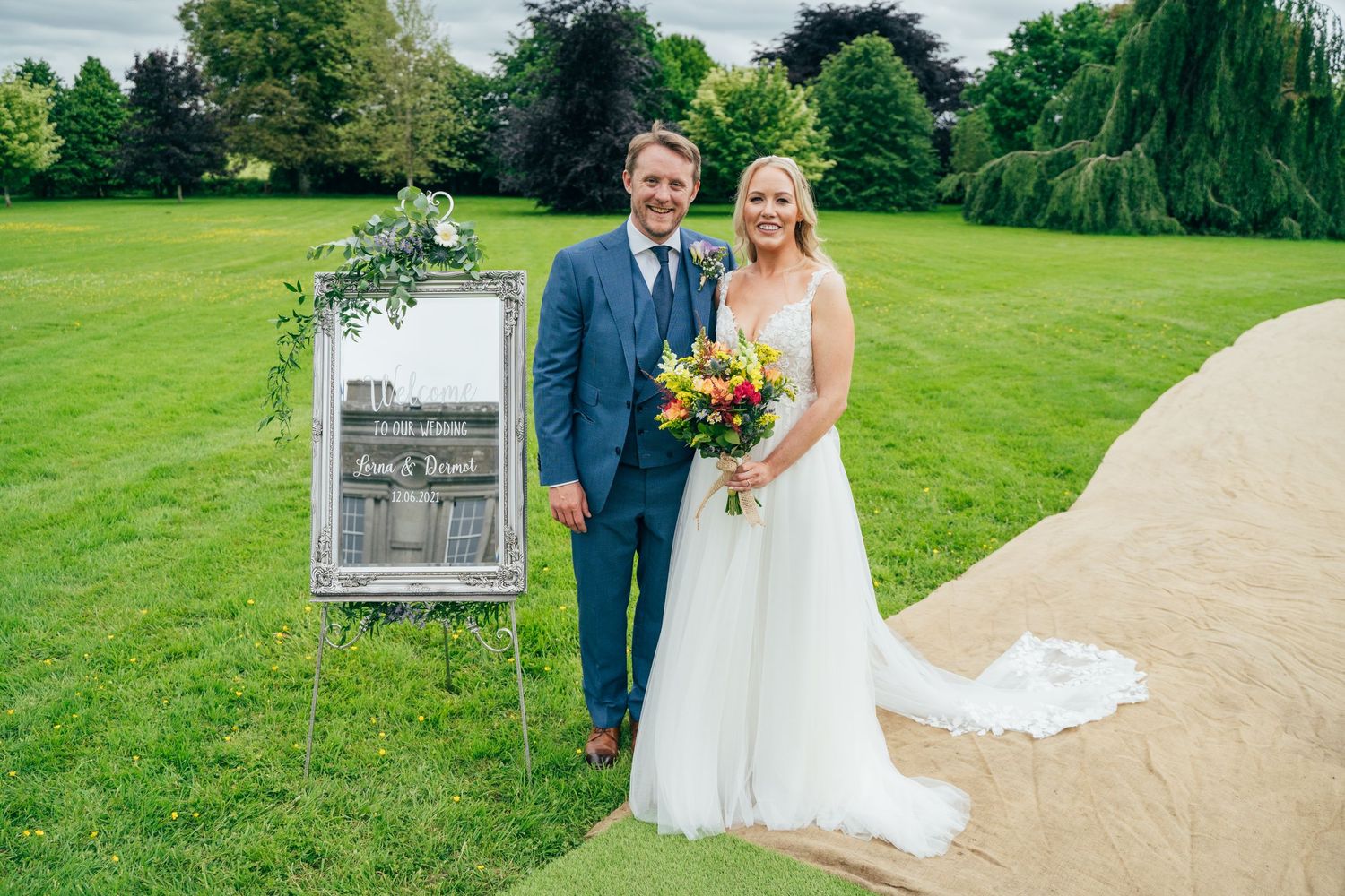 Bride and groom smiling together outdoors on lush green lawn beside decorative mirror sign at Bellinter house.