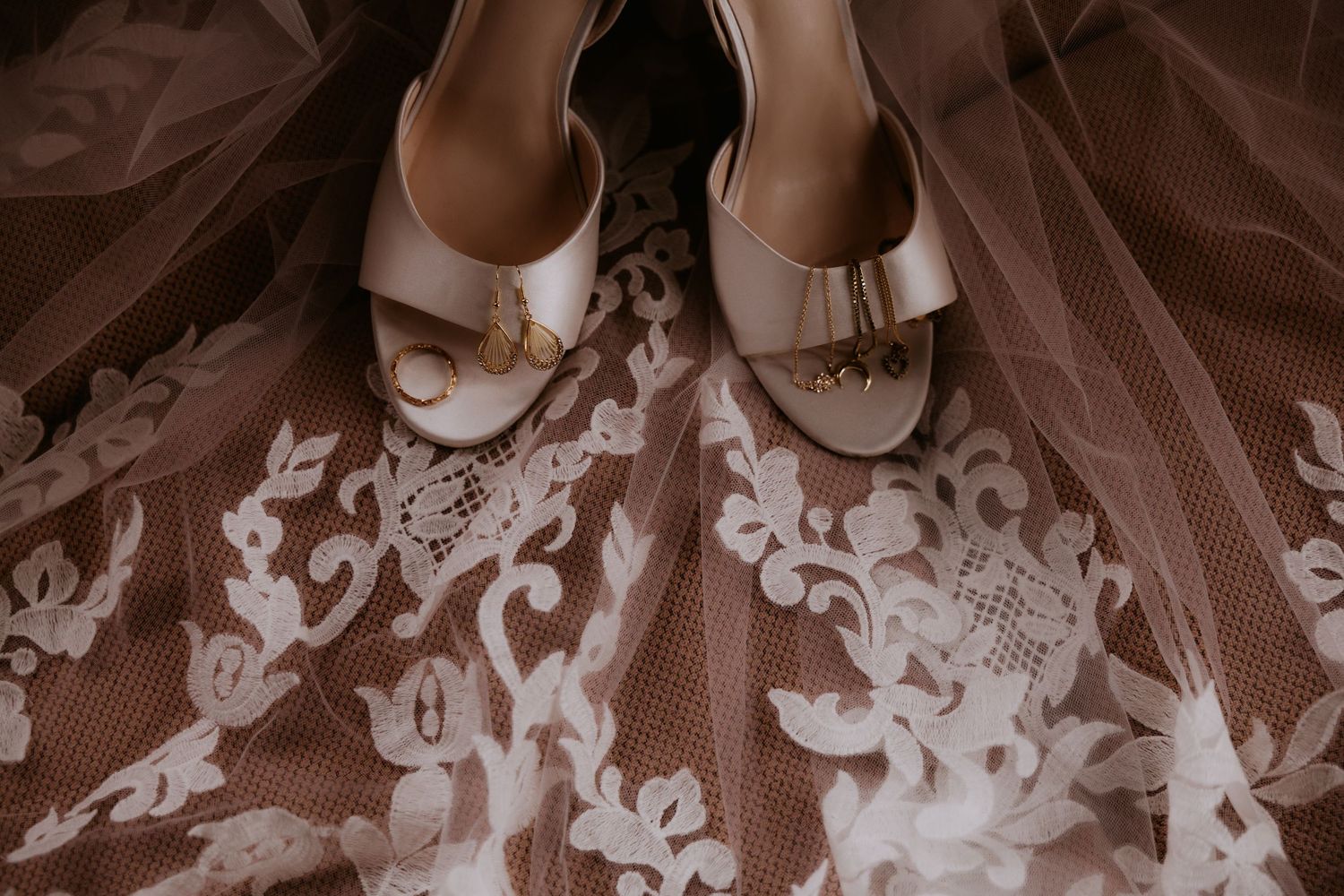 Elegant bridal heels with gold accents resting on intricate white lace wedding dress fabric.
