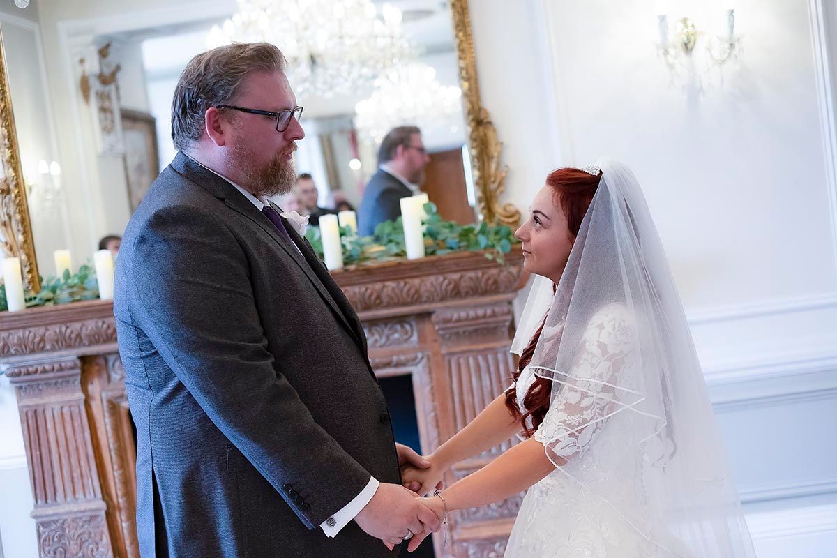 Bride and groom hold hands during indoor wedding ceremony at Auchen Castle