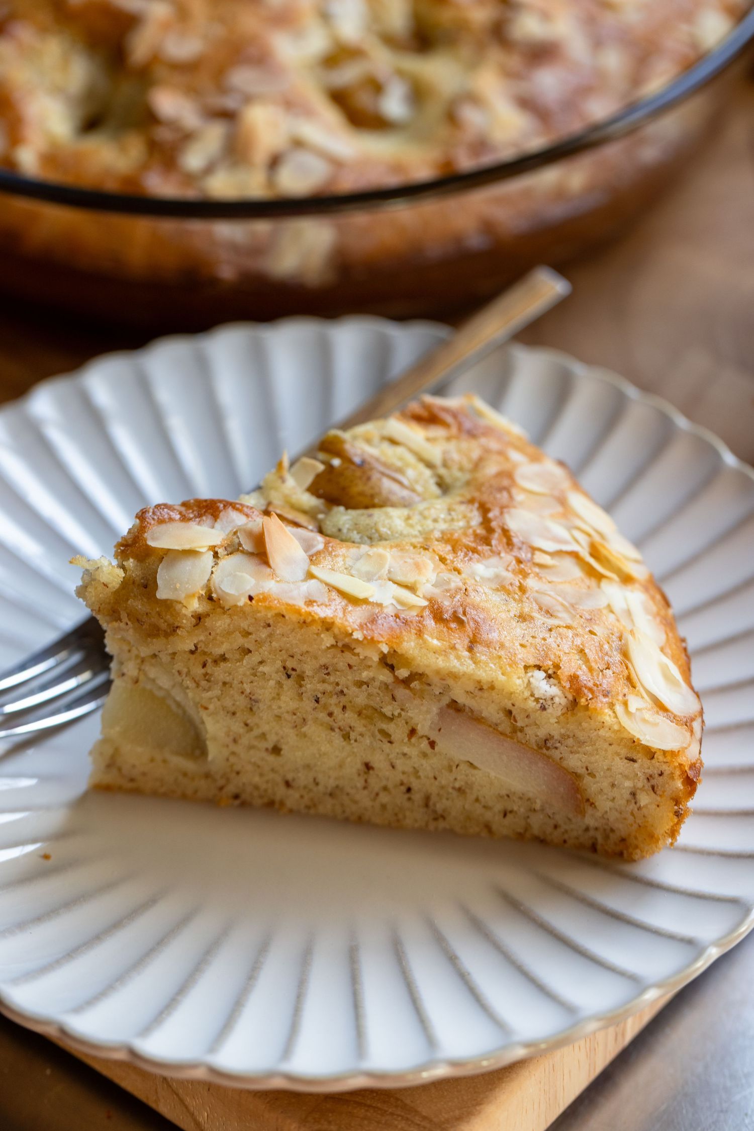 Golden peach loaf cake in parchment-lined pan, fresh peaches and pink flowers on wooden board.