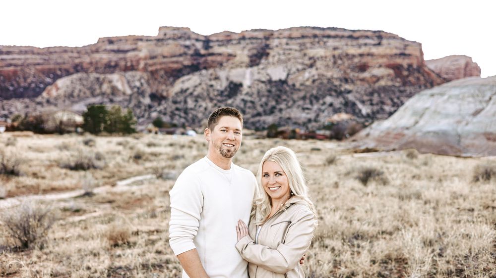 Close portrait of a smiling couple posing together with red rock mesas and desert scrub behind them.