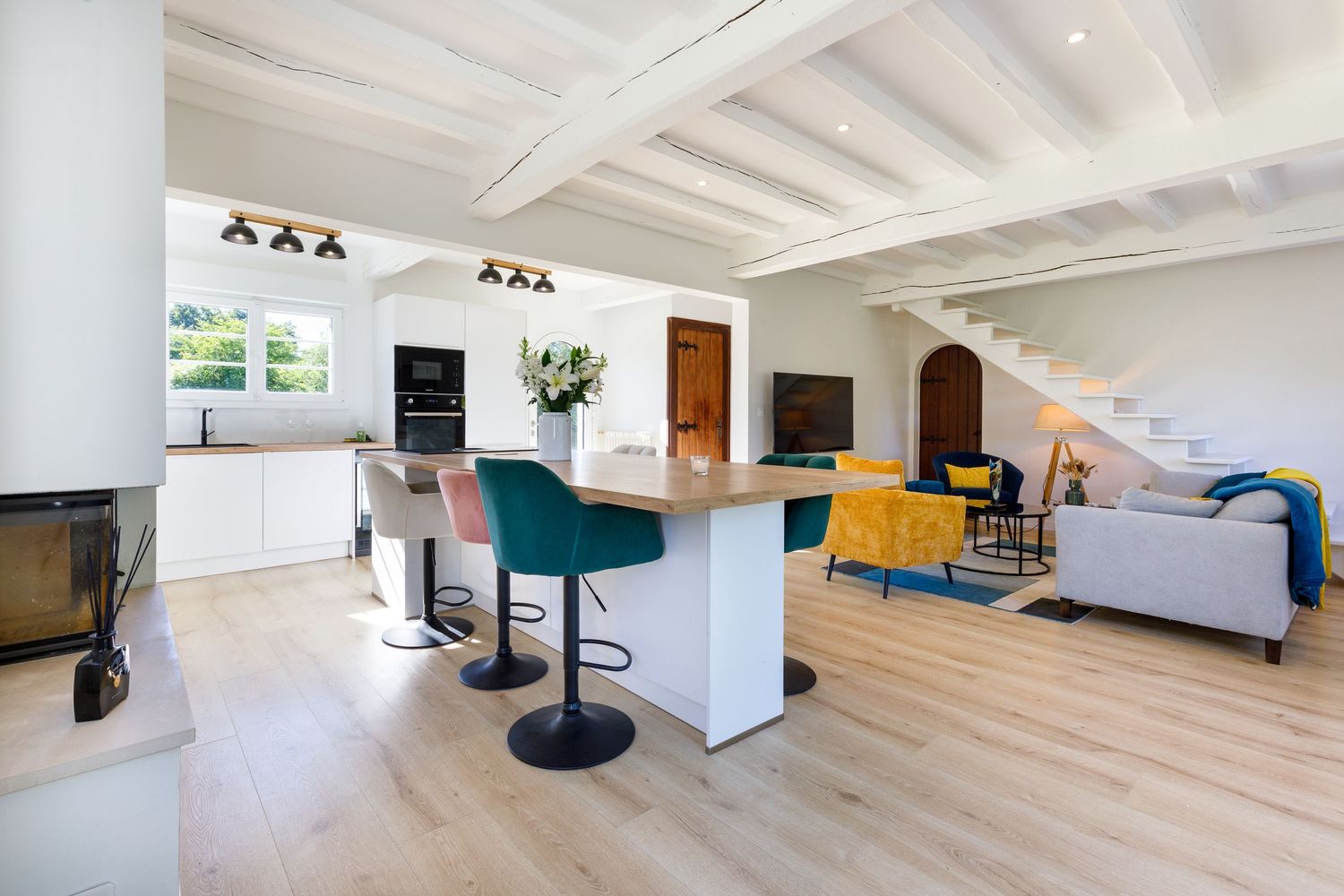 Cuisine et séjour avec plafonds à poutres blanches, tabourets de bar bleu et parquet en bois clair.